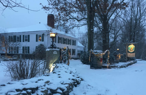 White house with dark shutters and roof in wintertime with gate lit up for the holidays.